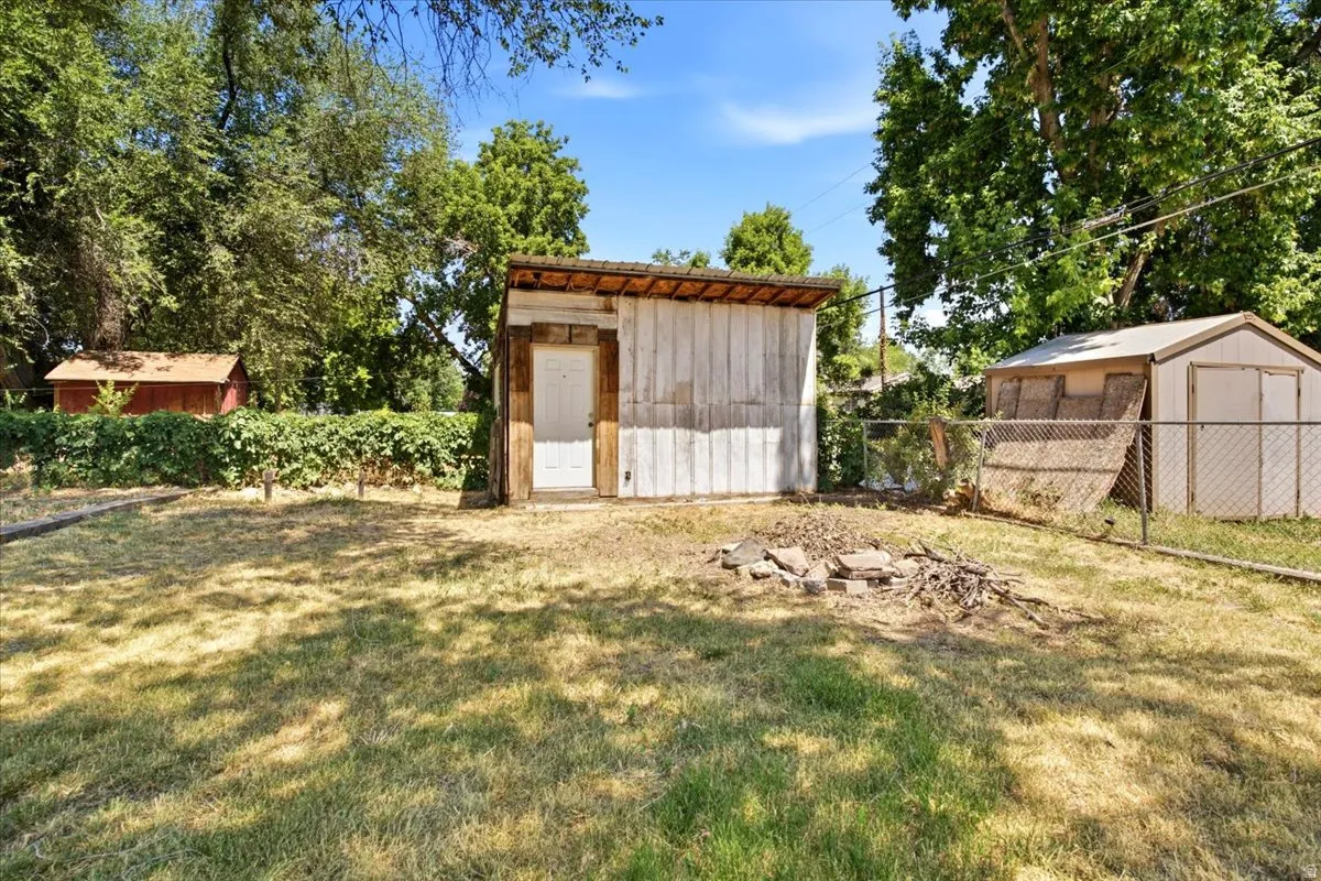 Expansive rear yard featuring a detached utility building with a white door, a smaller storage shed, and a chain-link fence