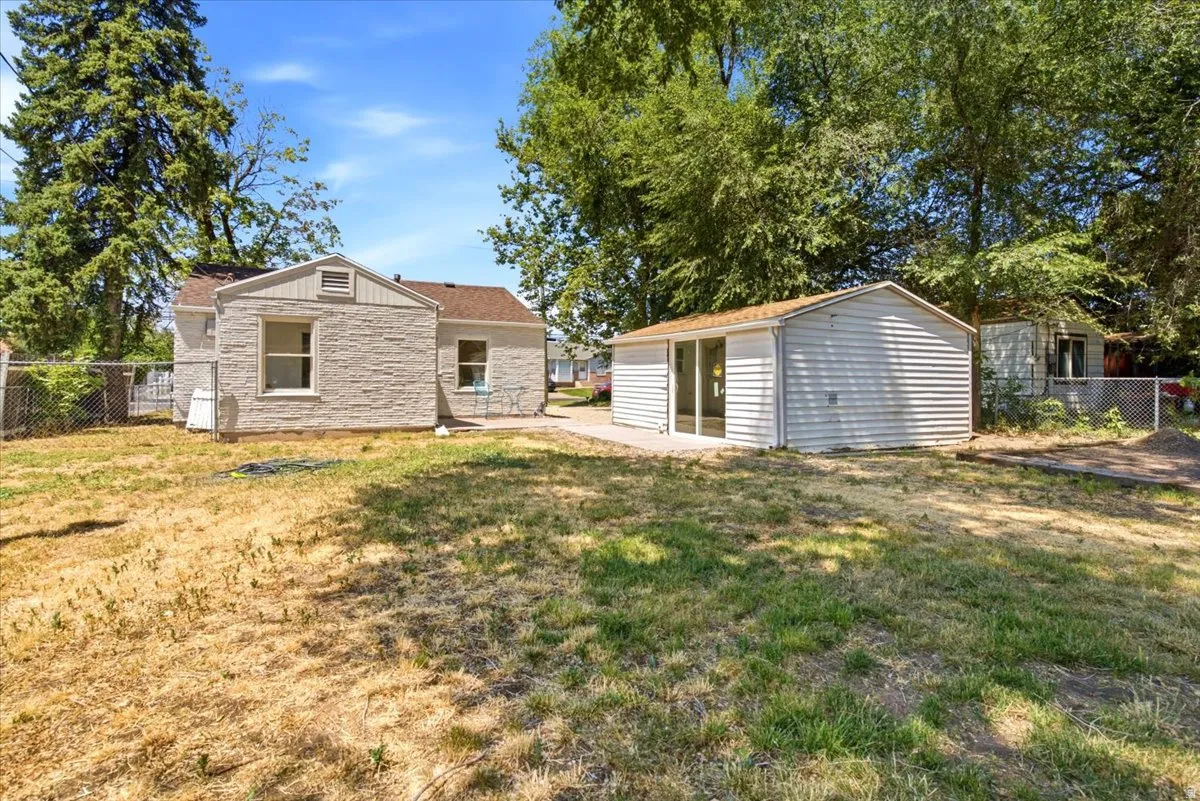 Expansive rear yard featuring a detached auxiliary structure with sliding glass doors, a chain-link fence perimeter, and mature trees