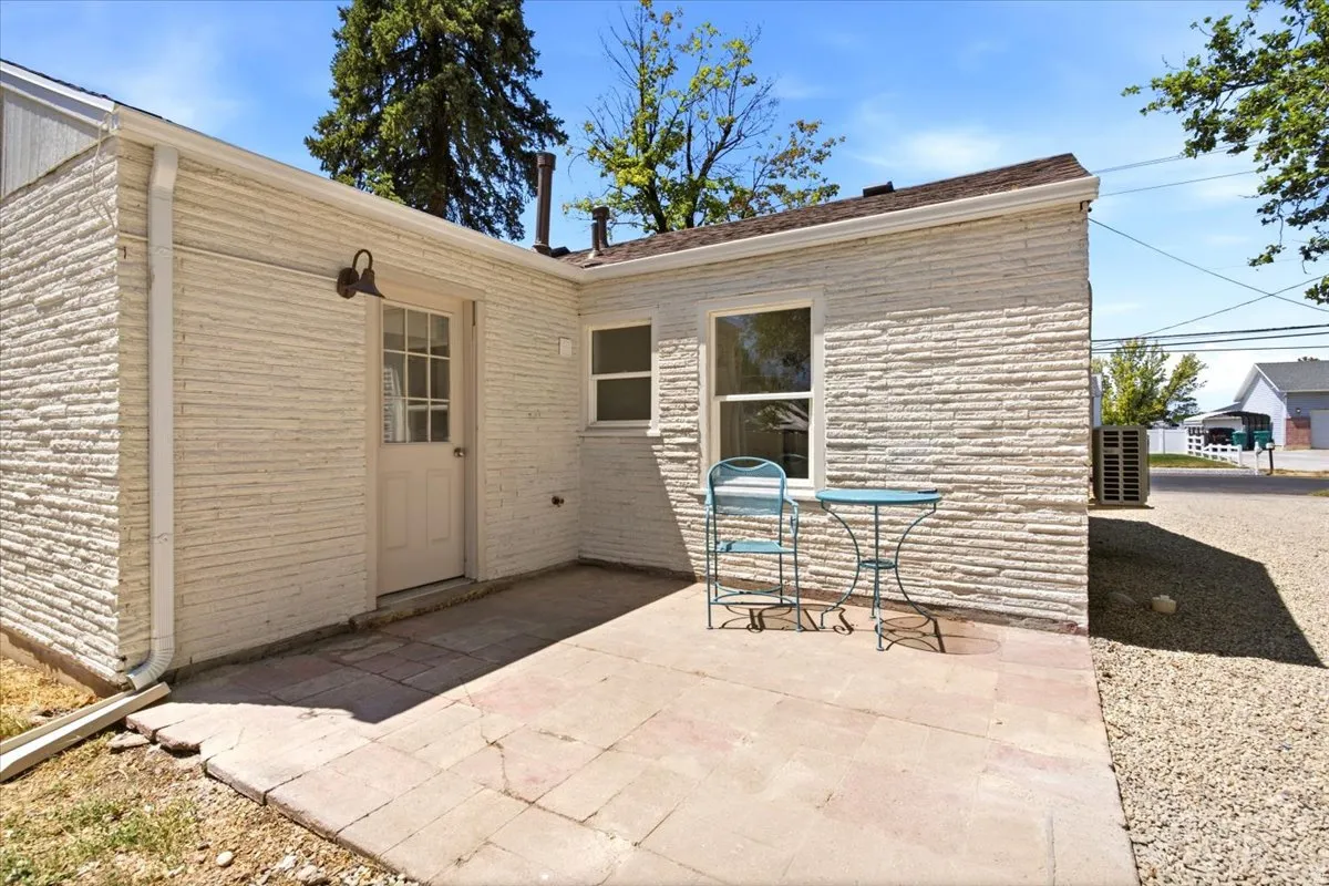 Exterior patio with a paver surface, textured white brick siding, a window, and an exterior door with glass panes