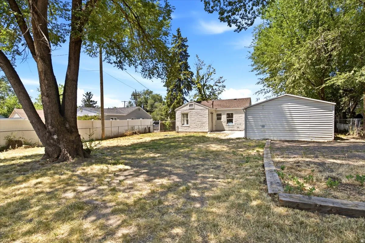 Expansive backyard featuring a mature tree, a detached garage with horizontal siding, and a stone-clad exterior on the main residence