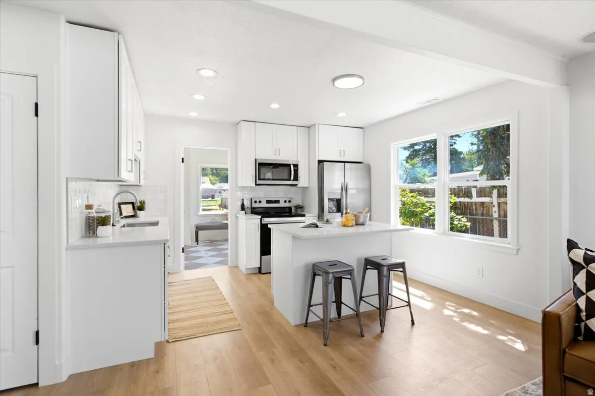 Bright kitchen featuring white cabinetry, stainless steel appliances, a center island with seating, wood-finish flooring, and ample natural light from multiple windows