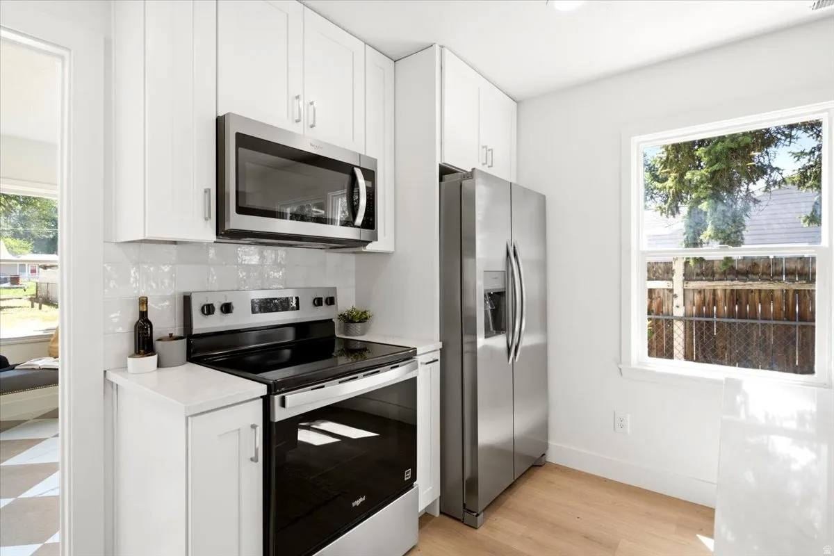 Kitchen featuring white shaker cabinetry, stainless steel appliances, light wood-finish flooring, and a white subway tile backsplash
