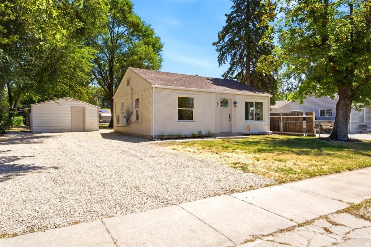 Single-story residence featuring a gravel driveway, a detached storage shed, and a brown shingle roof