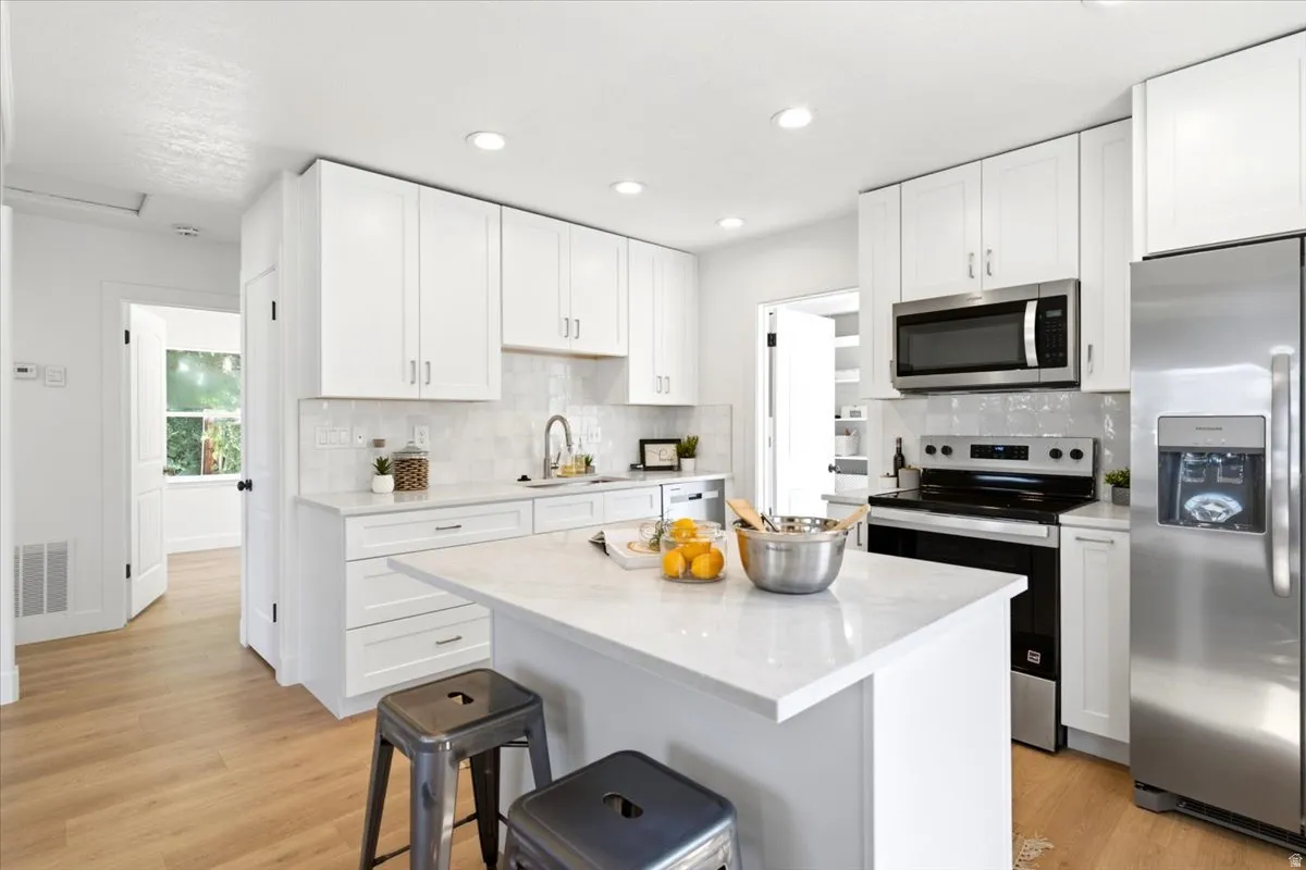 Kitchen featuring an island with countertop seating, white shaker cabinetry, stainless steel appliances, recessed lighting, and wood-finish flooring