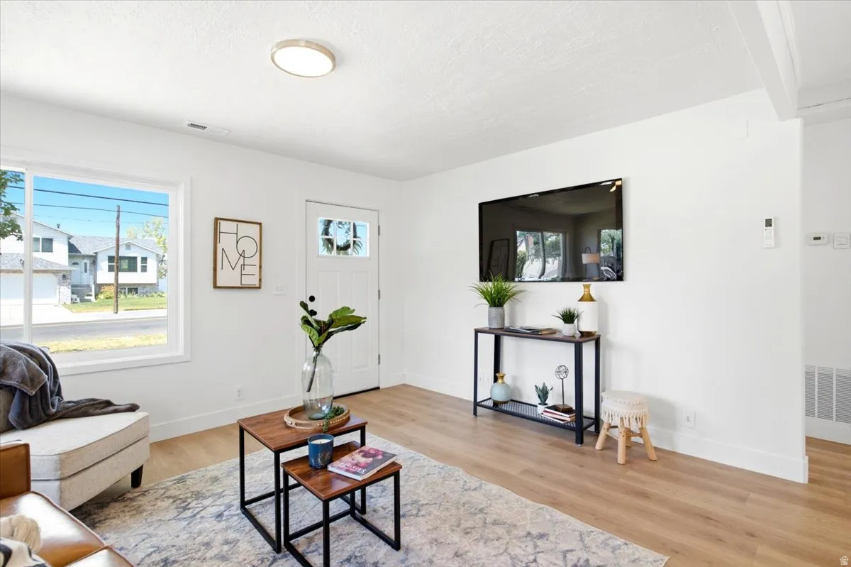 Bright living area featuring wood-finish flooring, white walls, and a front entry door with decorative glass