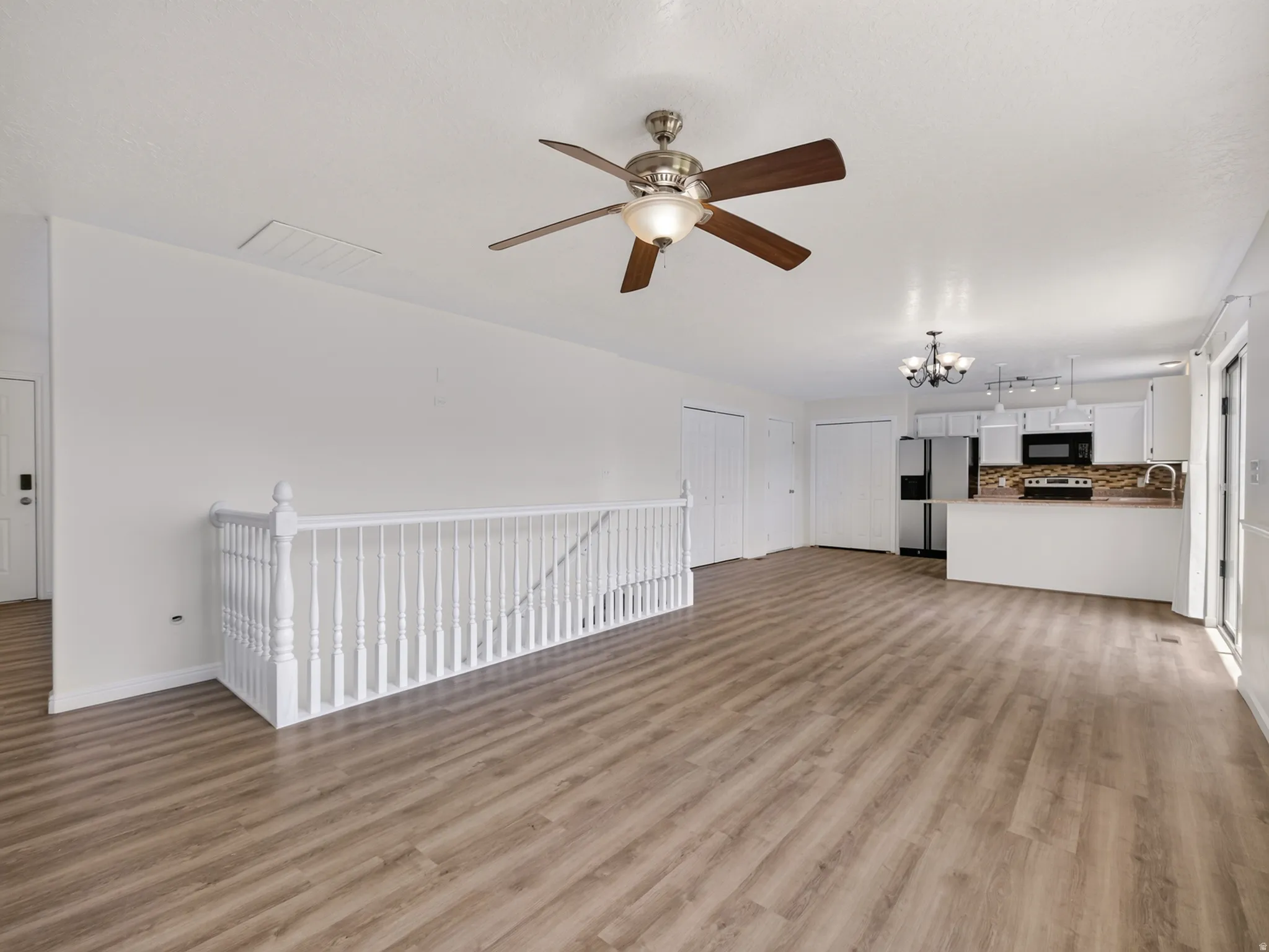Open-concept living area with wood-finish flooring, a contemporary ceiling fan, and a white baluster railing