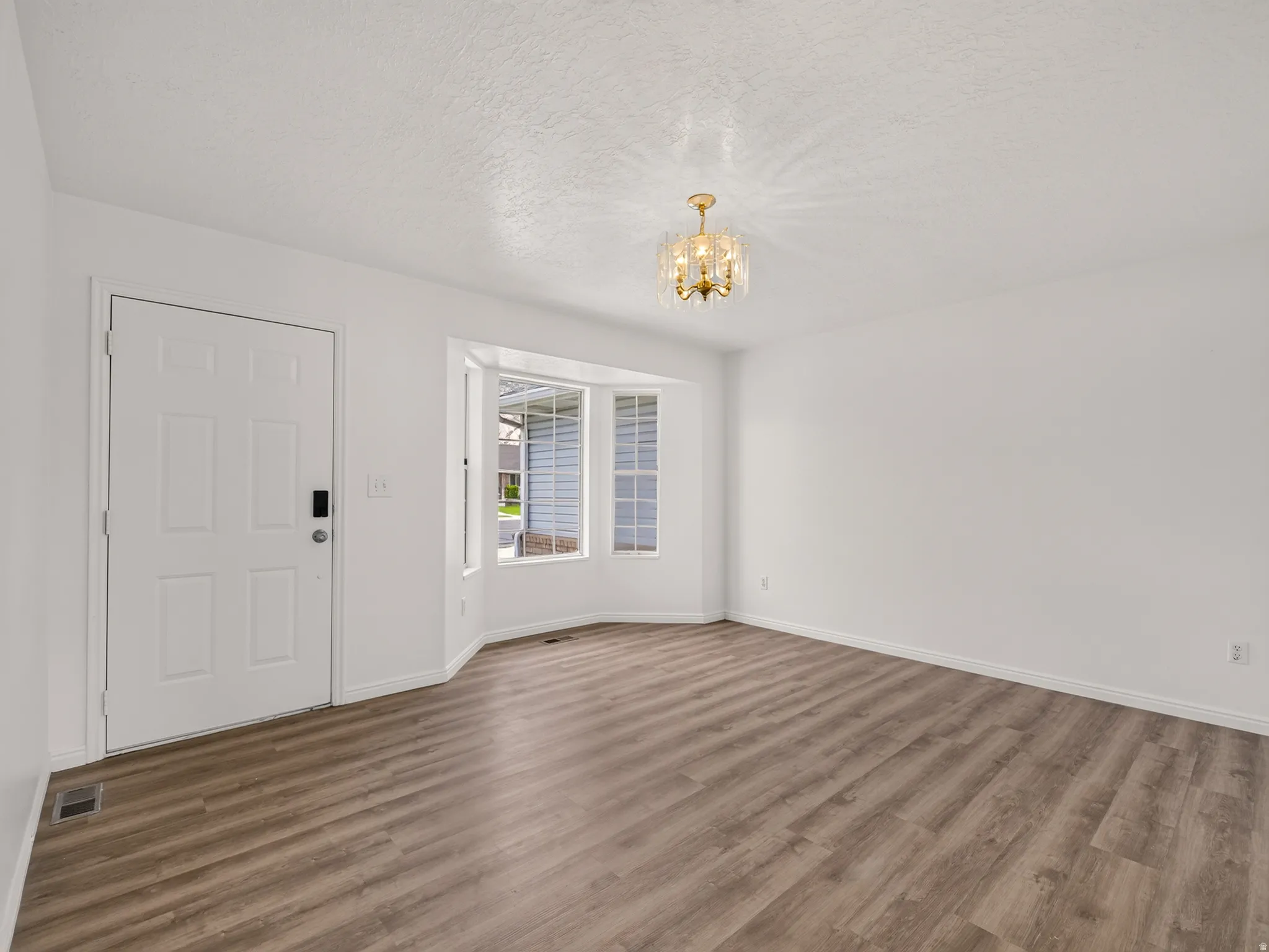 Inviting entry space featuring wood-finish flooring, a contemporary bay window, and a modern gold-tone chandelier