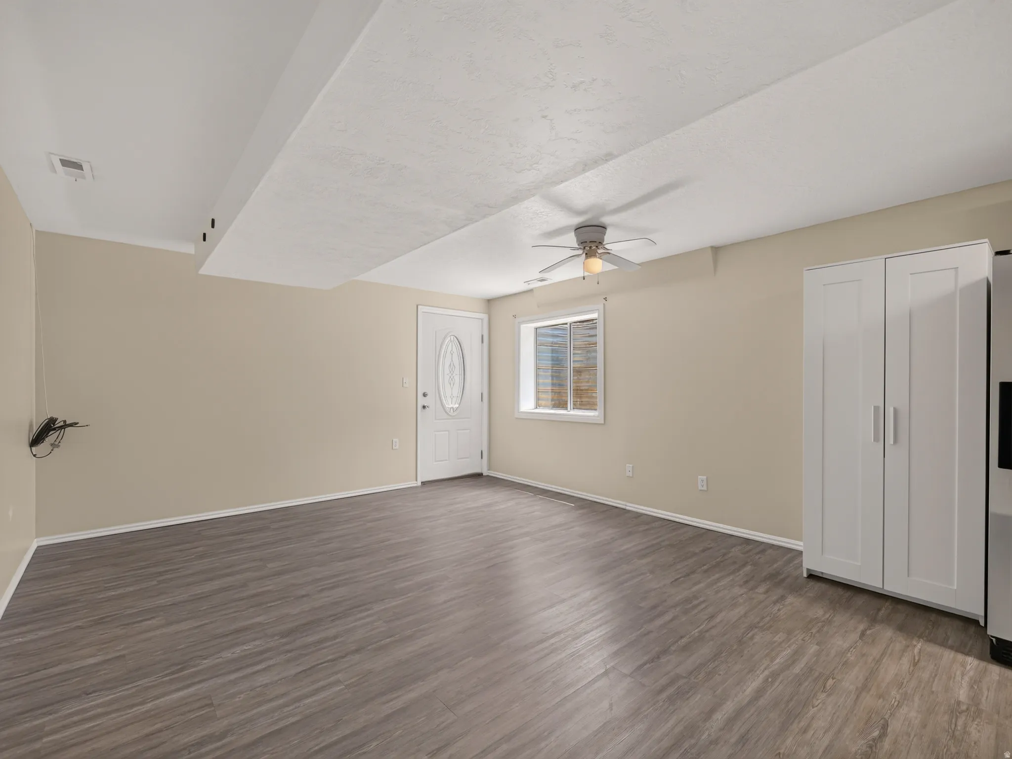 Spacious room with wood-finish flooring, neutral-toned walls, and a white entry door with an oval glass insert