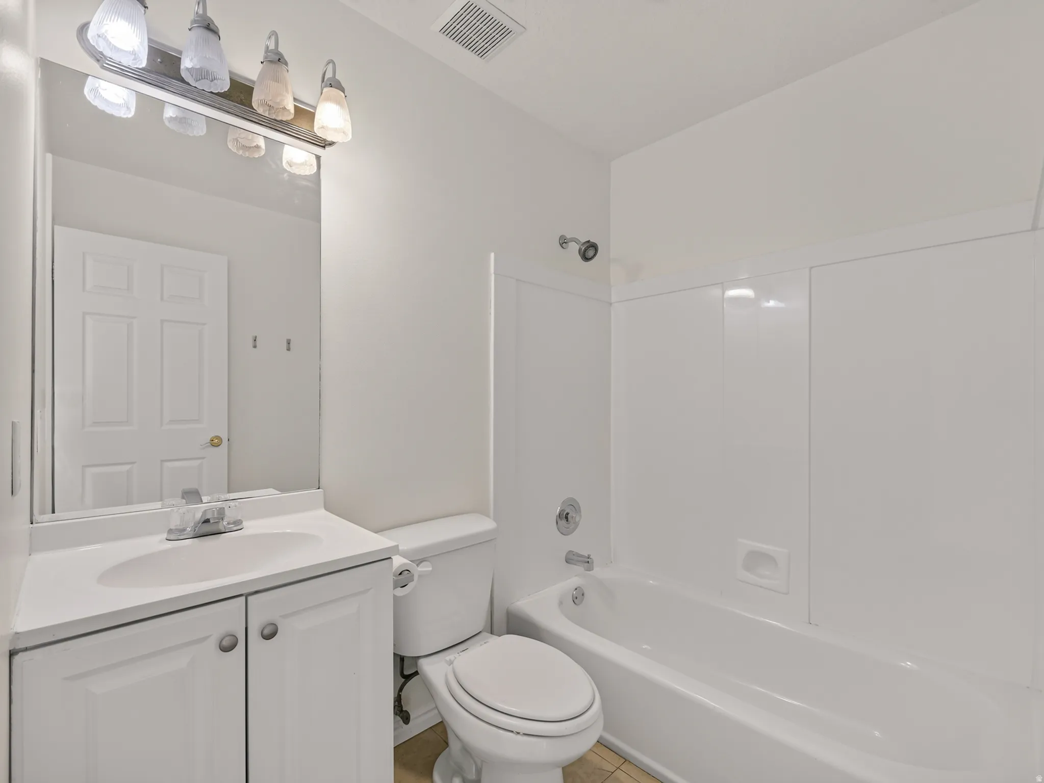 Full bathroom featuring a white vanity with integrated sink, coordinating white toilet, and a white tub with shower surround