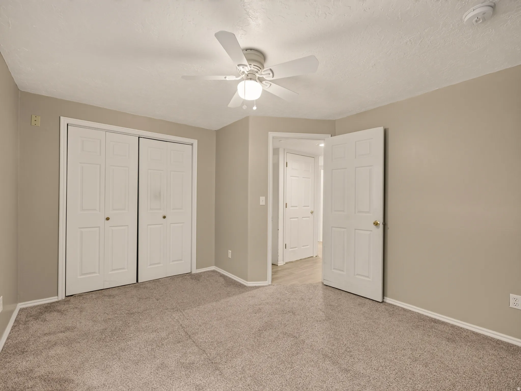 Neutral-toned room featuring a ceiling fan with integrated lighting, textured ceiling, and plush carpeting