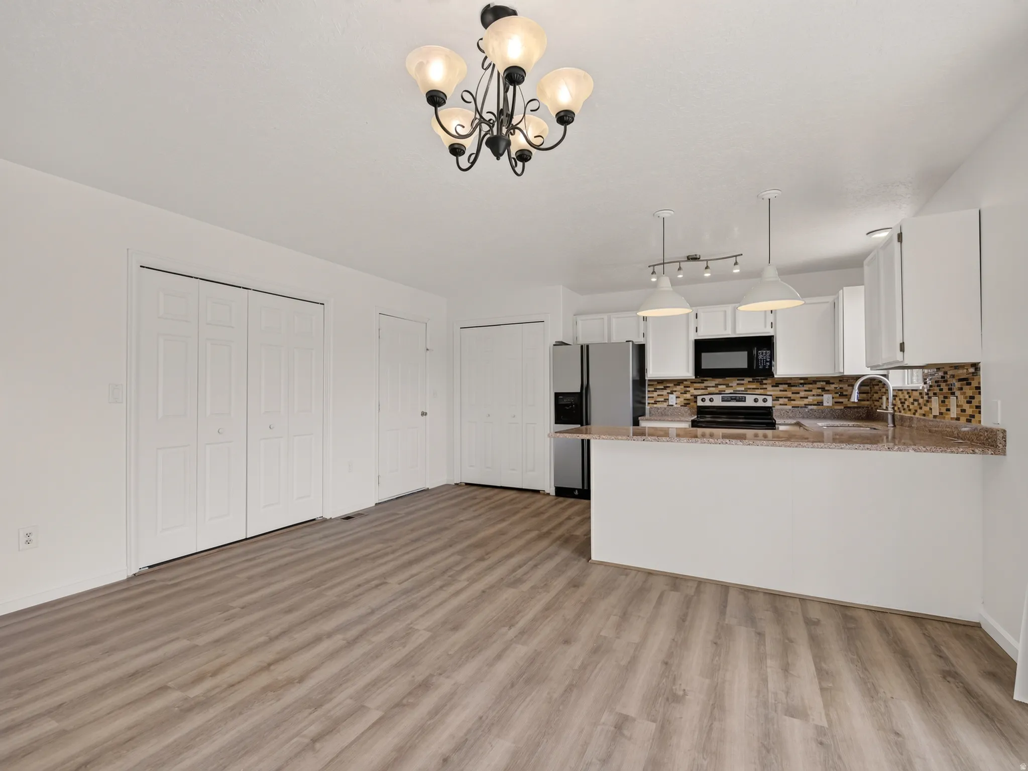 Open-concept kitchen and living area featuring wood-finish flooring, white cabinetry, stainless steel appliances, a mosaic tile backsplash, and a breakfast bar