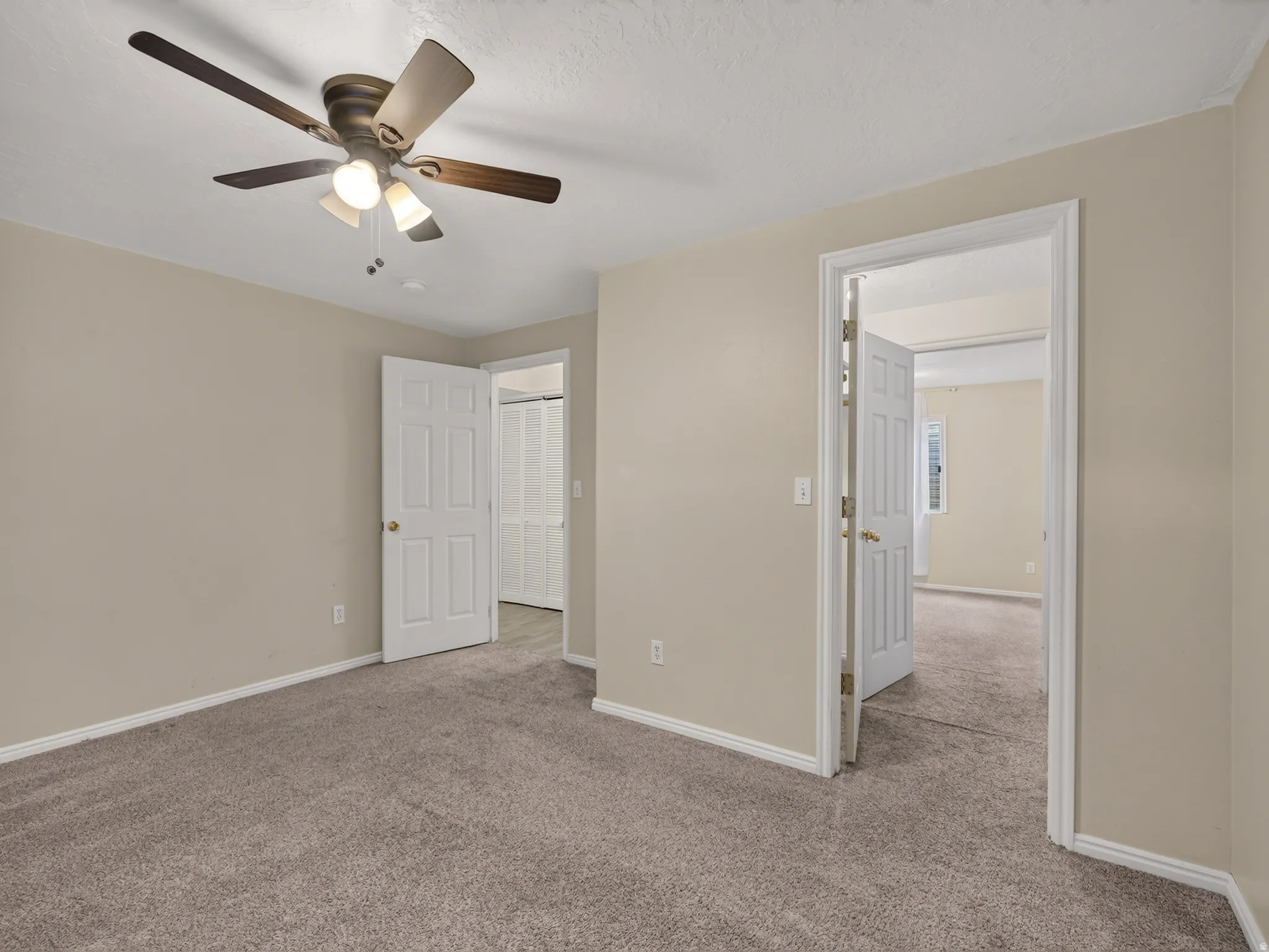 Neutral-toned walls and plush carpeting in this room with a ceiling fan with integrated lighting