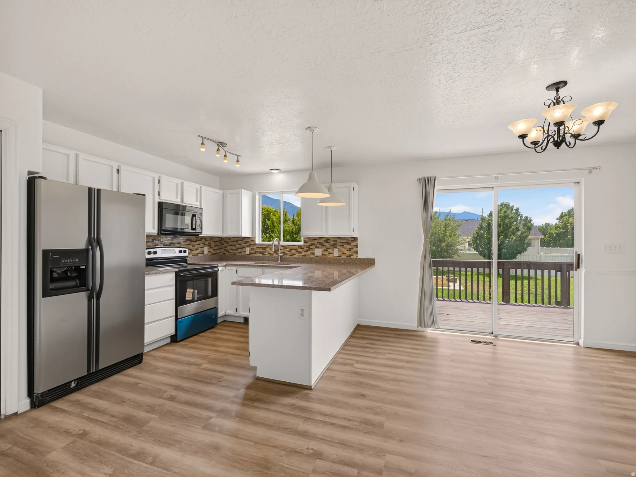 Open-concept kitchen and dining area featuring wood-finish flooring, white cabinetry, a large kitchen island with a stone-look countertop, stainless steel appliances, and sliding glass doors opening to a private deck