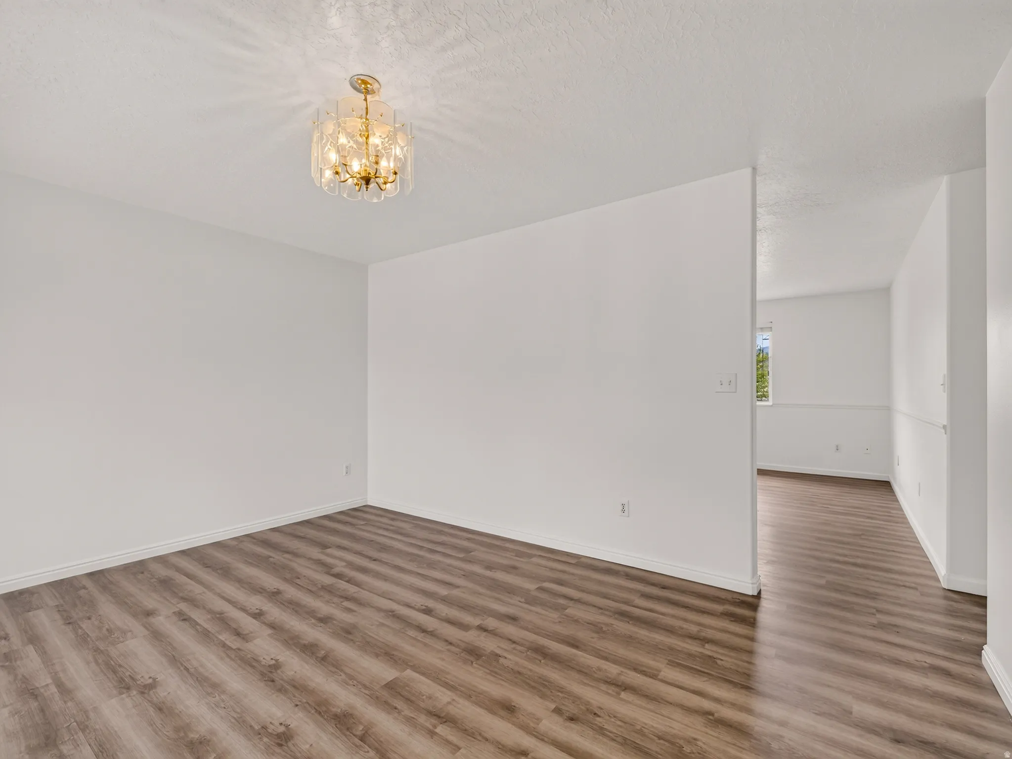 Spacious room featuring wood-finish flooring, white walls, and a contemporary crystal chandelier