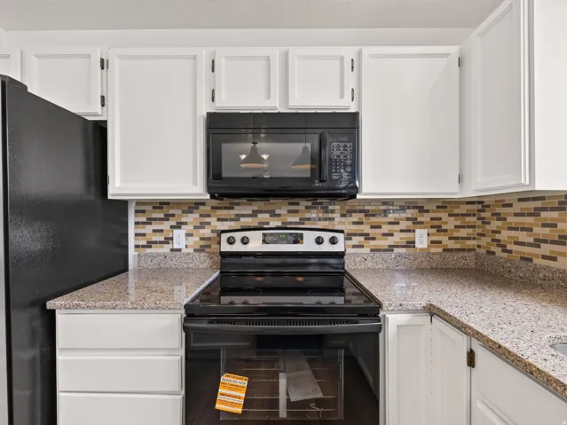 Kitchen featuring granite-style countertops, white cabinetry, and a mosaic tile backsplash