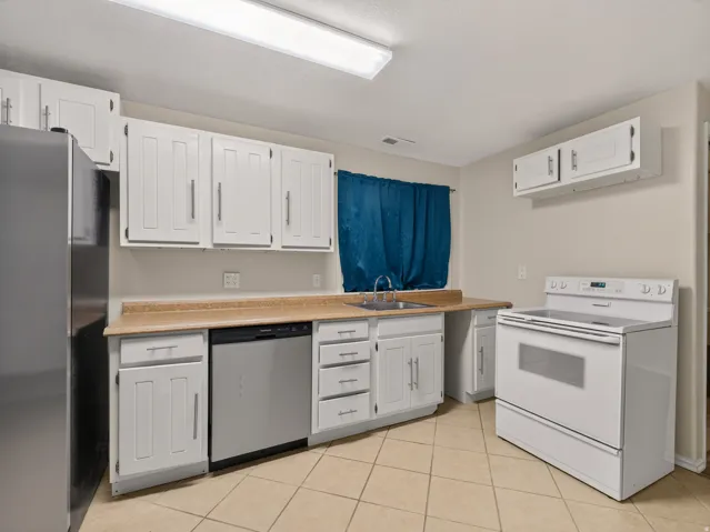 Kitchen featuring white cabinetry, light countertops, tile flooring, a stainless steel dishwasher, and a white electric range