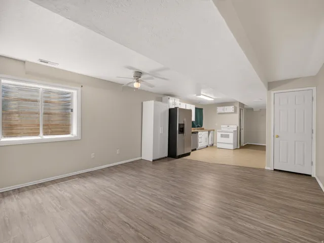 Spacious room featuring wood-finish flooring, a ceiling fan, and a window with a window well