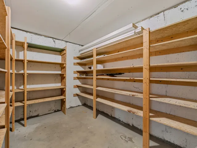 Utility room featuring extensive built-in wooden shelving, exposed concrete walls, and a concrete floor