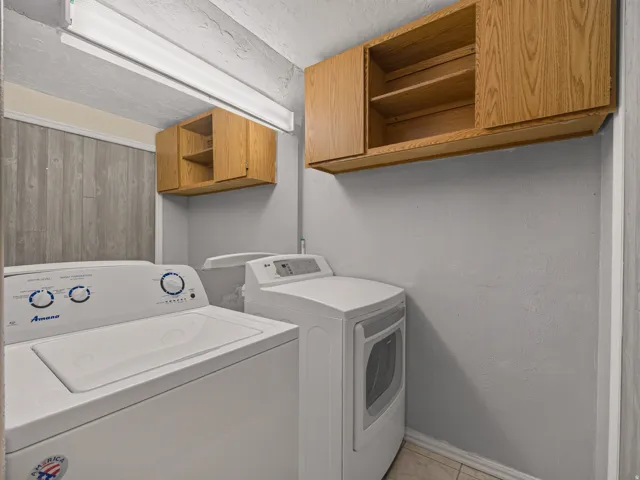 Dedicated laundry area featuring a washer and dryer, wood-finish wall paneling, and upper cabinetry for storage