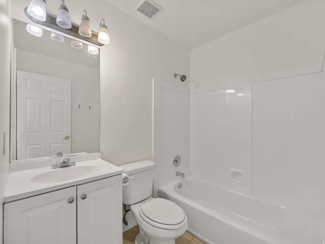 Full bathroom featuring a white vanity with integrated sink, coordinating white toilet, and a white tub with shower surround