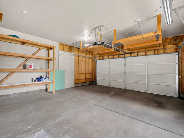 Spacious garage featuring a concrete floor, built-in wooden shelving, and overhead storage platforms