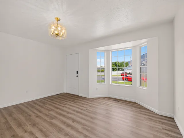 Bright living space with wood-finish flooring, a bay window with multiple panes, a contemporary ceiling light fixture, and a white paneled door with modern hardware