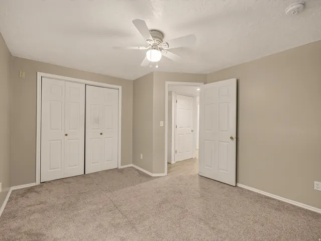 Neutral-toned room featuring a ceiling fan with integrated lighting, textured ceiling, and plush carpeting