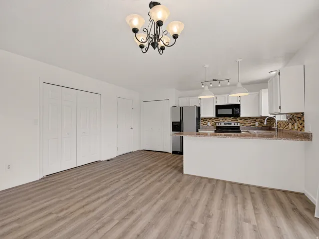 Open-concept kitchen and living area featuring wood-finish flooring, white cabinetry, stainless steel appliances, a mosaic tile backsplash, and a breakfast bar