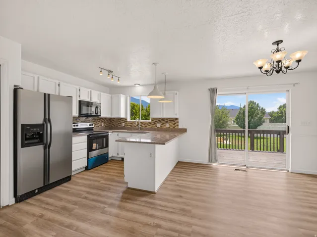 Open-concept kitchen and dining area featuring wood-finish flooring, white cabinetry, a large kitchen island with a stone-look countertop, stainless steel appliances, and sliding glass doors opening to a private deck