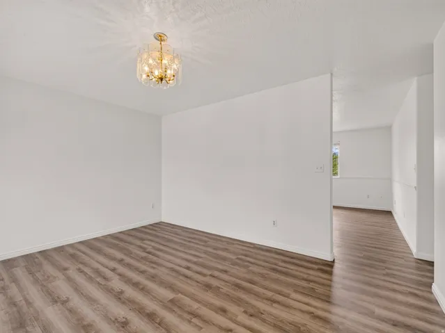 Spacious room featuring wood-finish flooring, white walls, and a contemporary crystal chandelier
