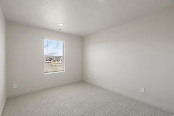 Neutral tone walls with light gray carpeting, recessed ceiling lighting, and a single window with horizontal blinds