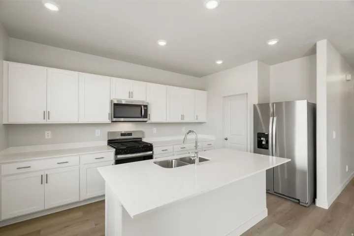 Modern kitchen featuring an island with double sinks, stainless steel appliances, white cabinetry, and light-tone wood-finish flooring