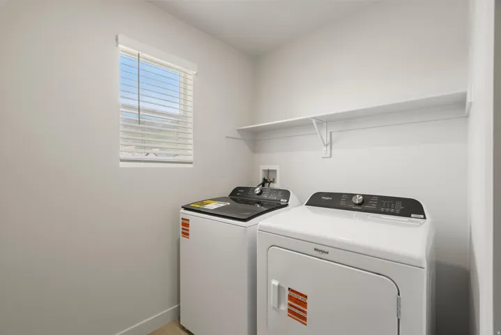 Dedicated laundry area featuring a window with blinds, upper storage shelving, and light wood-finish flooring