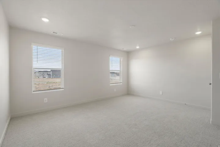 Spacious room featuring neutral carpeting, light-toned wall paint, and multiple recessed ceiling lights