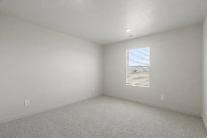 Spacious room featuring light gray walls, plush gray carpeting, recessed lighting, and a window with horizontal blinds
