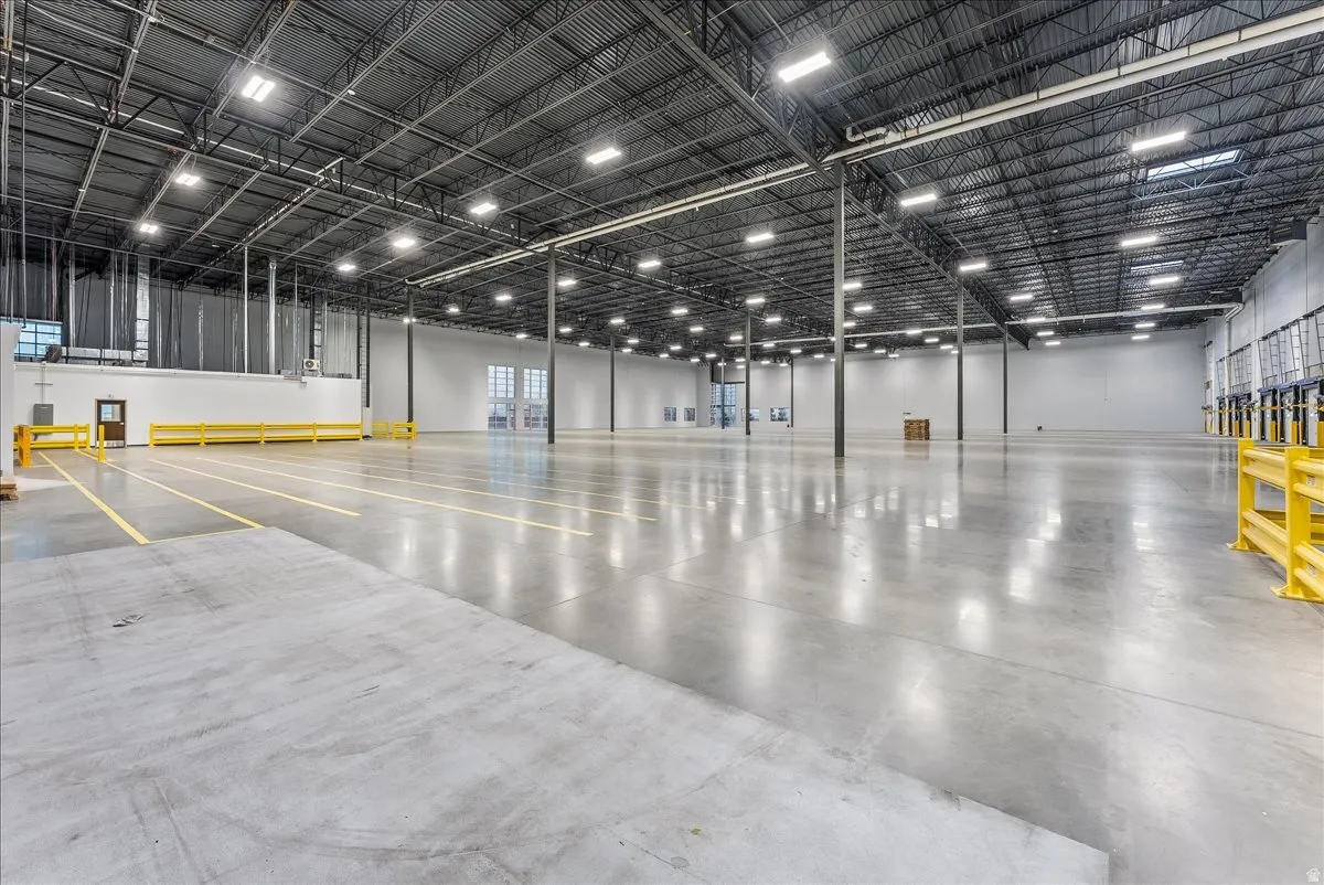 Expansive industrial interior featuring polished concrete flooring, high ceilings with exposed metal trusses, integrated overhead lighting, and multiple loading dock access points