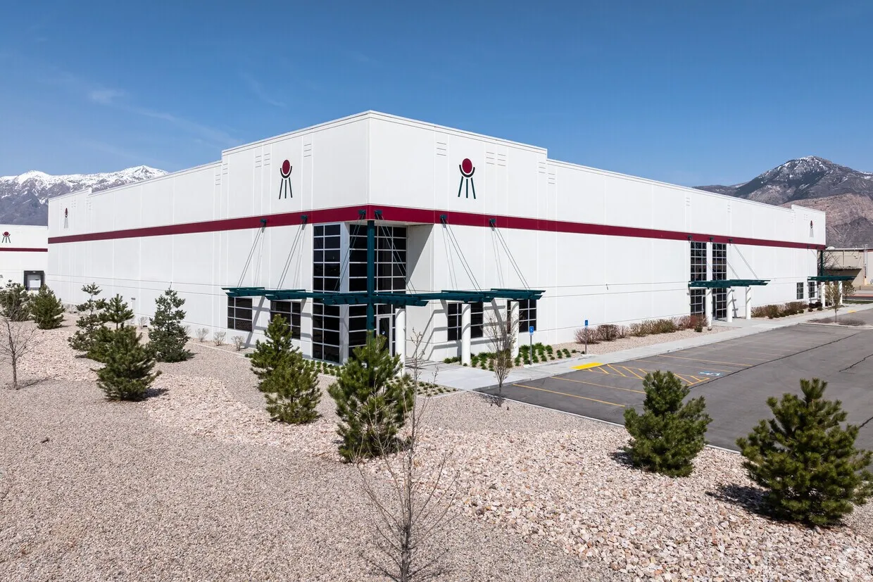 Modern commercial building featuring a white facade with red accents, large glass entrance, multiple overhead awnings, a gravel landscaping, and paved parking