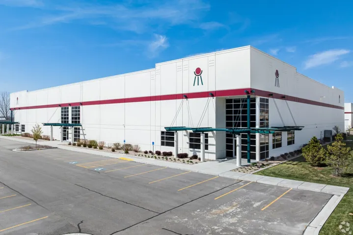 Commercial building with a white facade and red band accents, featuring multiple large storefront windows, covered entryways, and a dedicated parking area