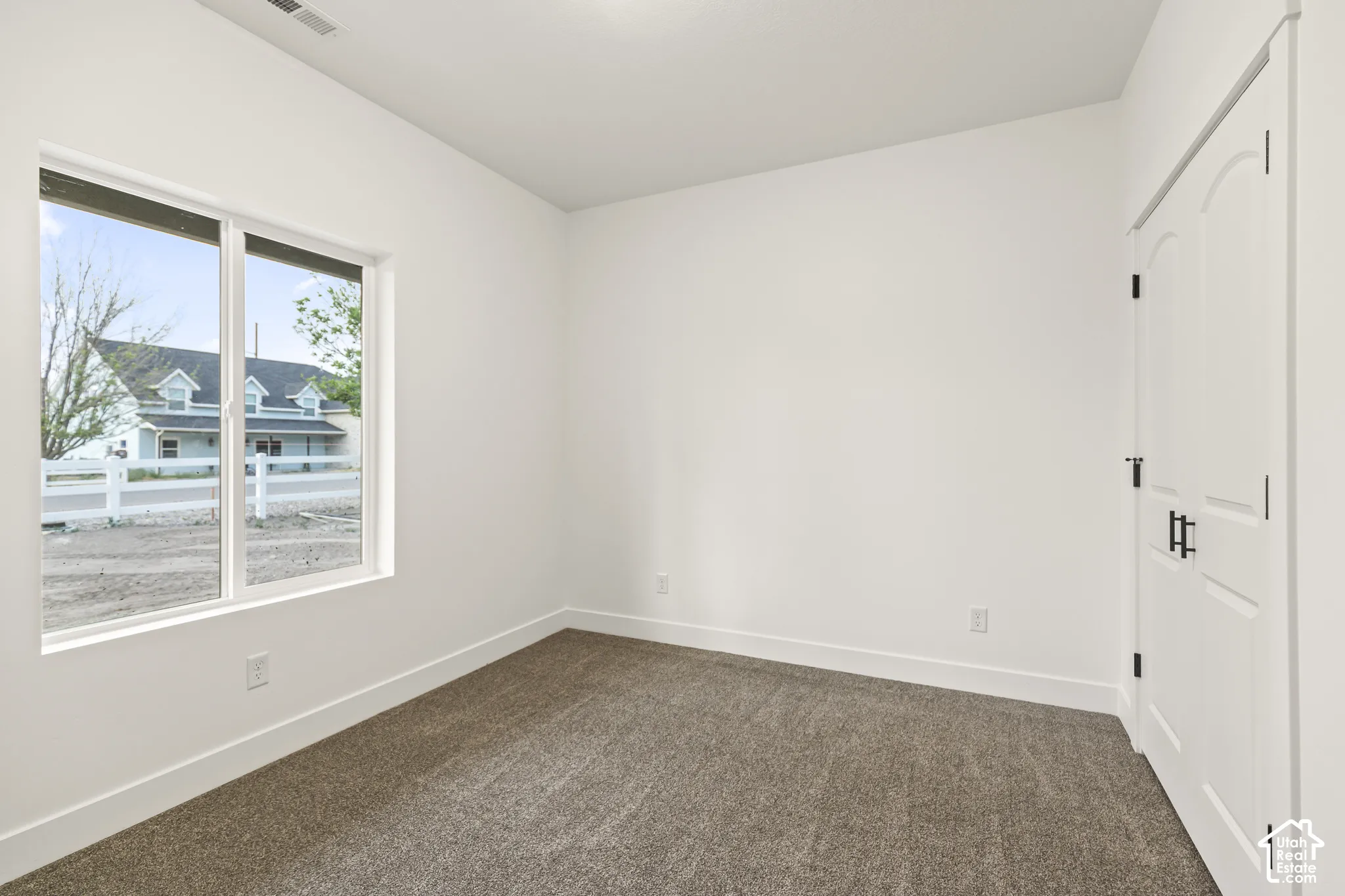 Room featuring a window with exterior views, carpeted flooring, white walls, and a white interior door with black hardware