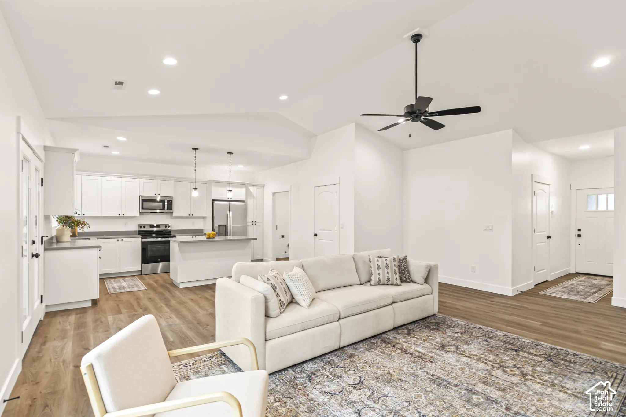 Vaulted ceilings, wood-finish flooring, recessed lighting, kitchen with island and white cabinetry, and matte black ceiling fan