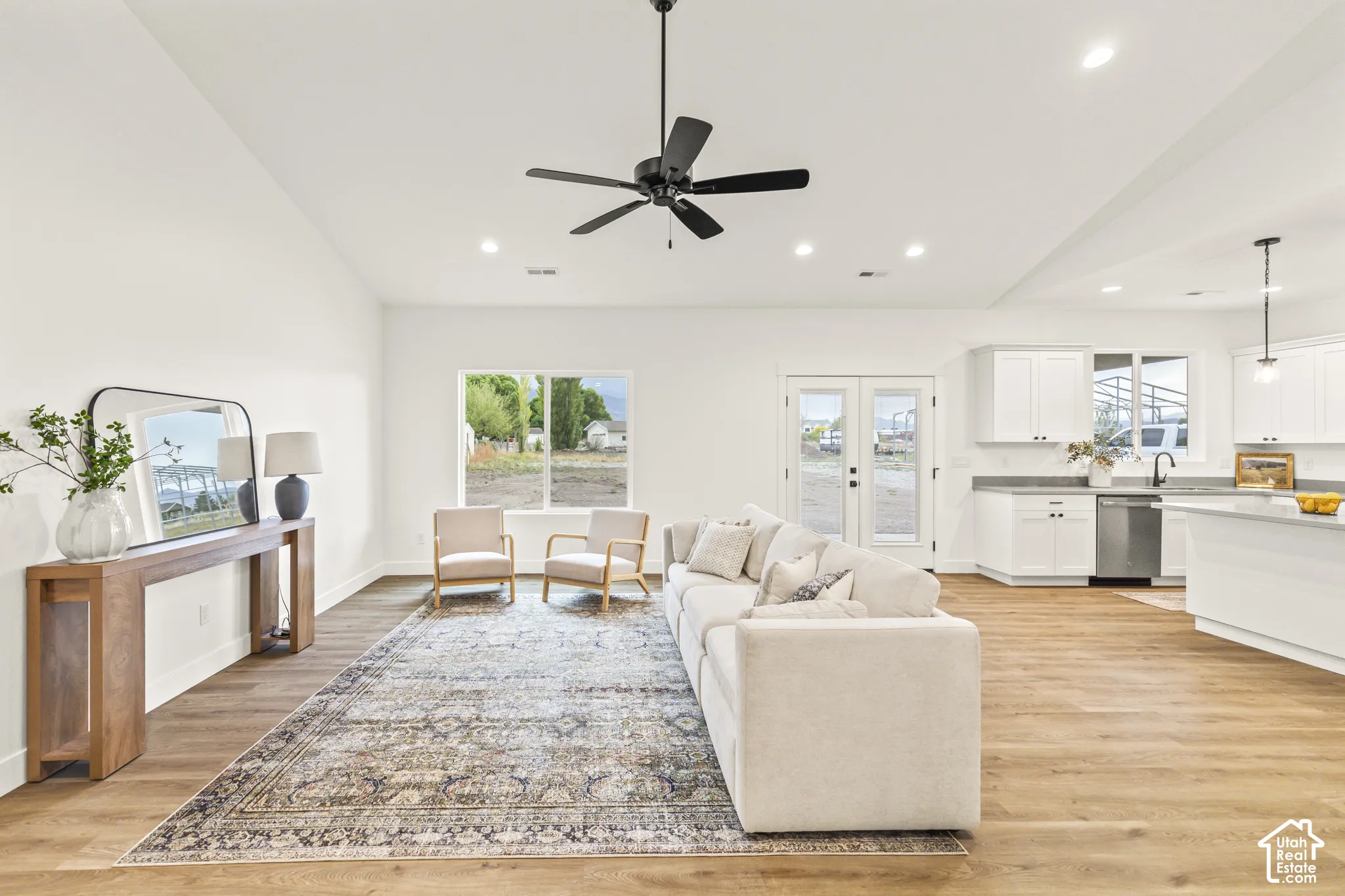 Open-concept living space featuring vaulted ceilings, wood-finish flooring, a matte black ceiling fan, recessed lighting, and white cabinetry with a coordinating island