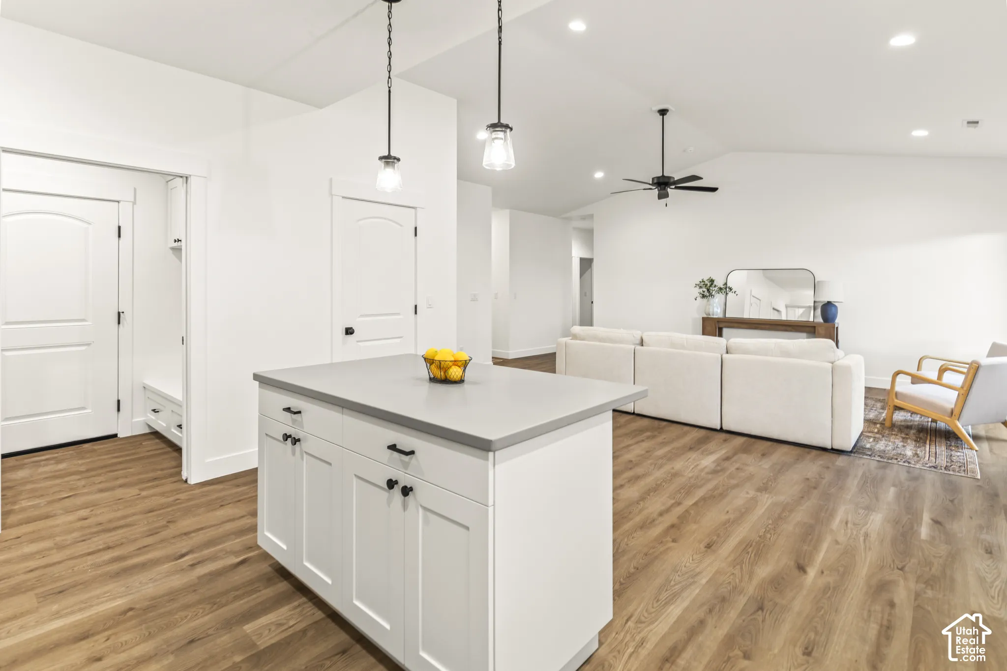 Kitchen island featuring a solid-surface countertop and shaker-style cabinetry, complemented by wood-finish flooring, vaulted ceilings, and matte black pendant lighting