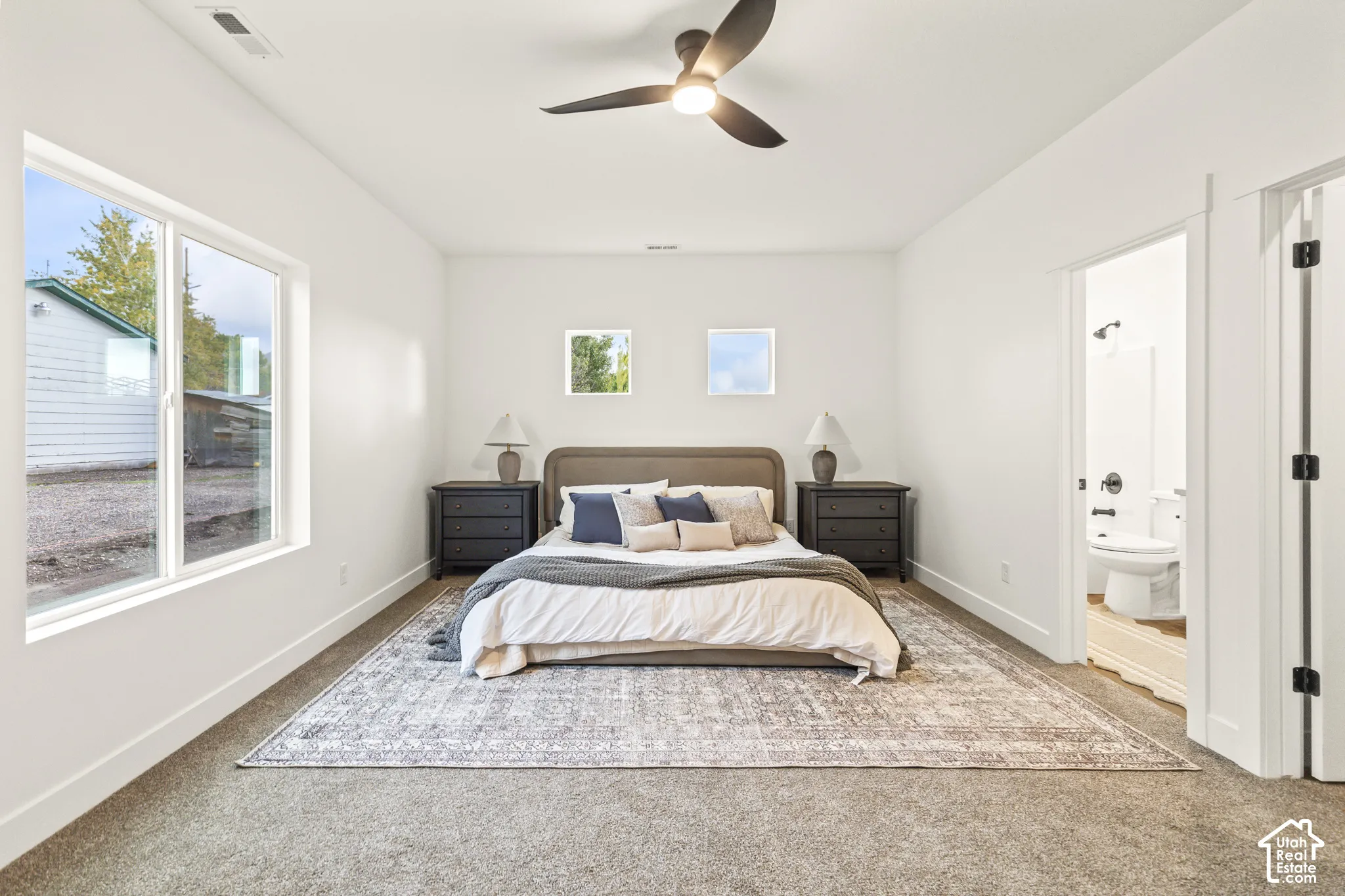 Spacious interior featuring neutral wall tones, wall-to-wall carpeting, a multi-blade ceiling fan, and large windows
