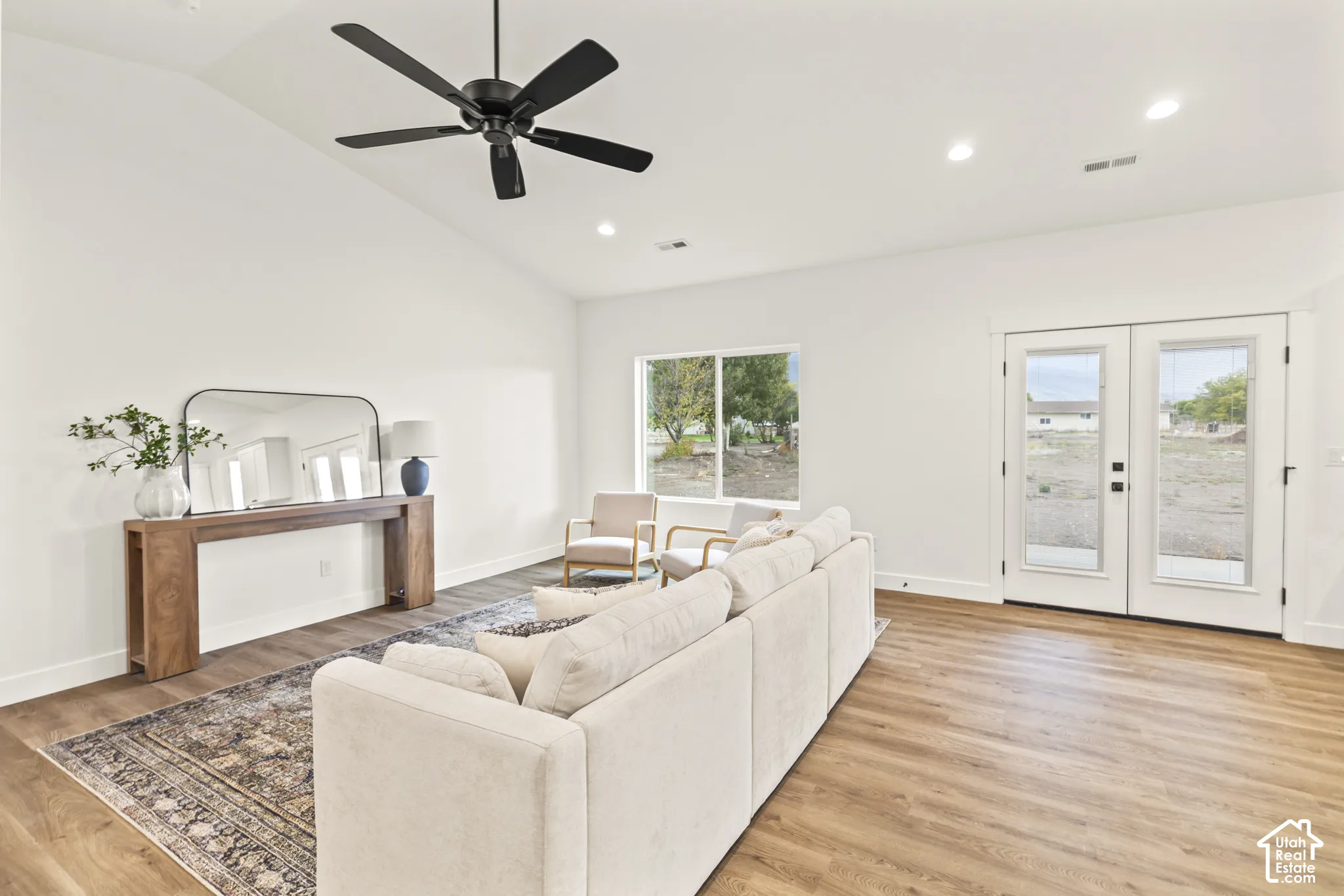 Living area featuring vaulted ceilings, wood-finish flooring, a matte black ceiling fan, recessed lighting, and double-pane glass entry doors
