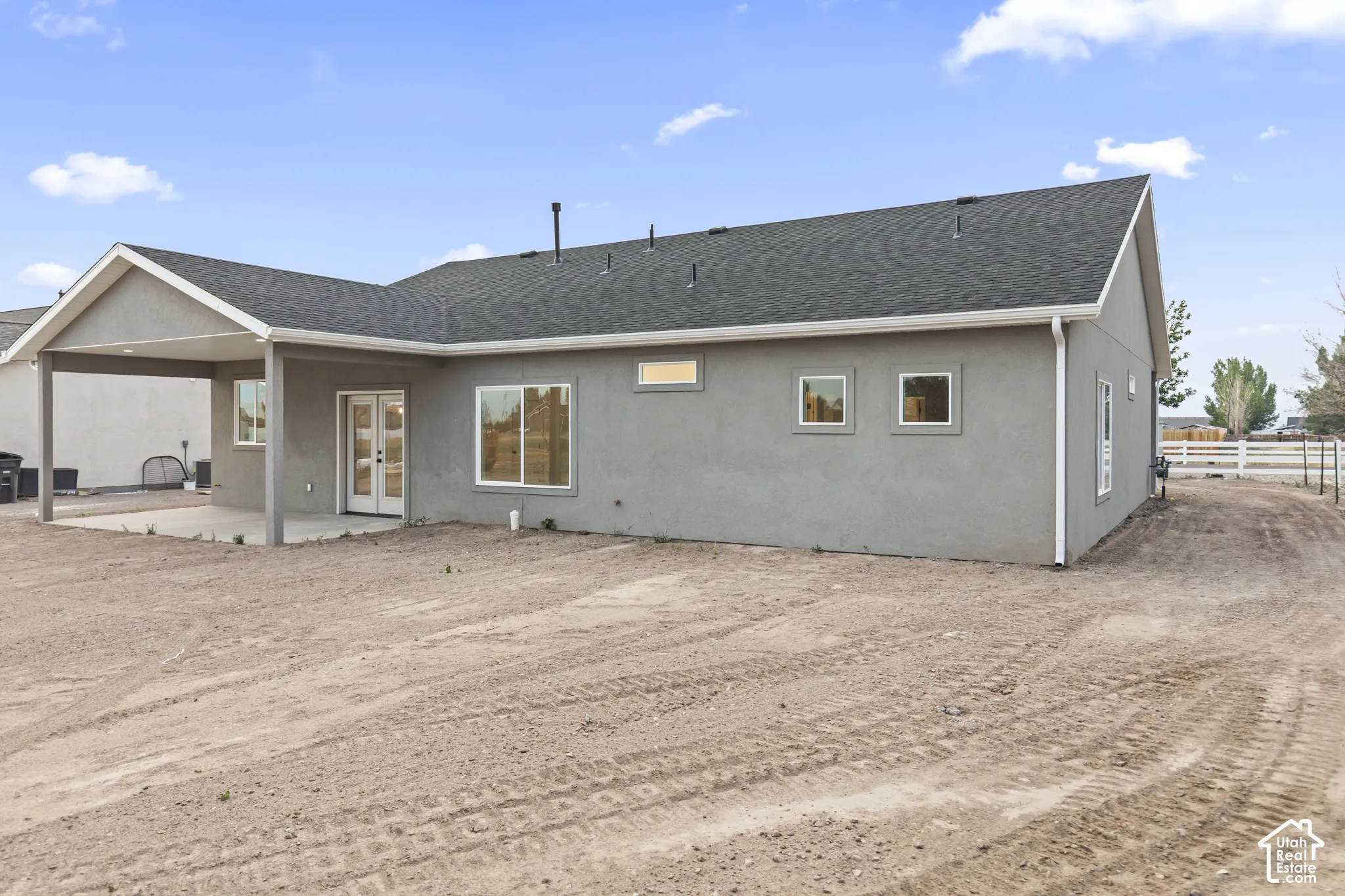 Rear exterior featuring stucco siding, a covered patio, a dark shingle roof, double patio doors, and multiple windows