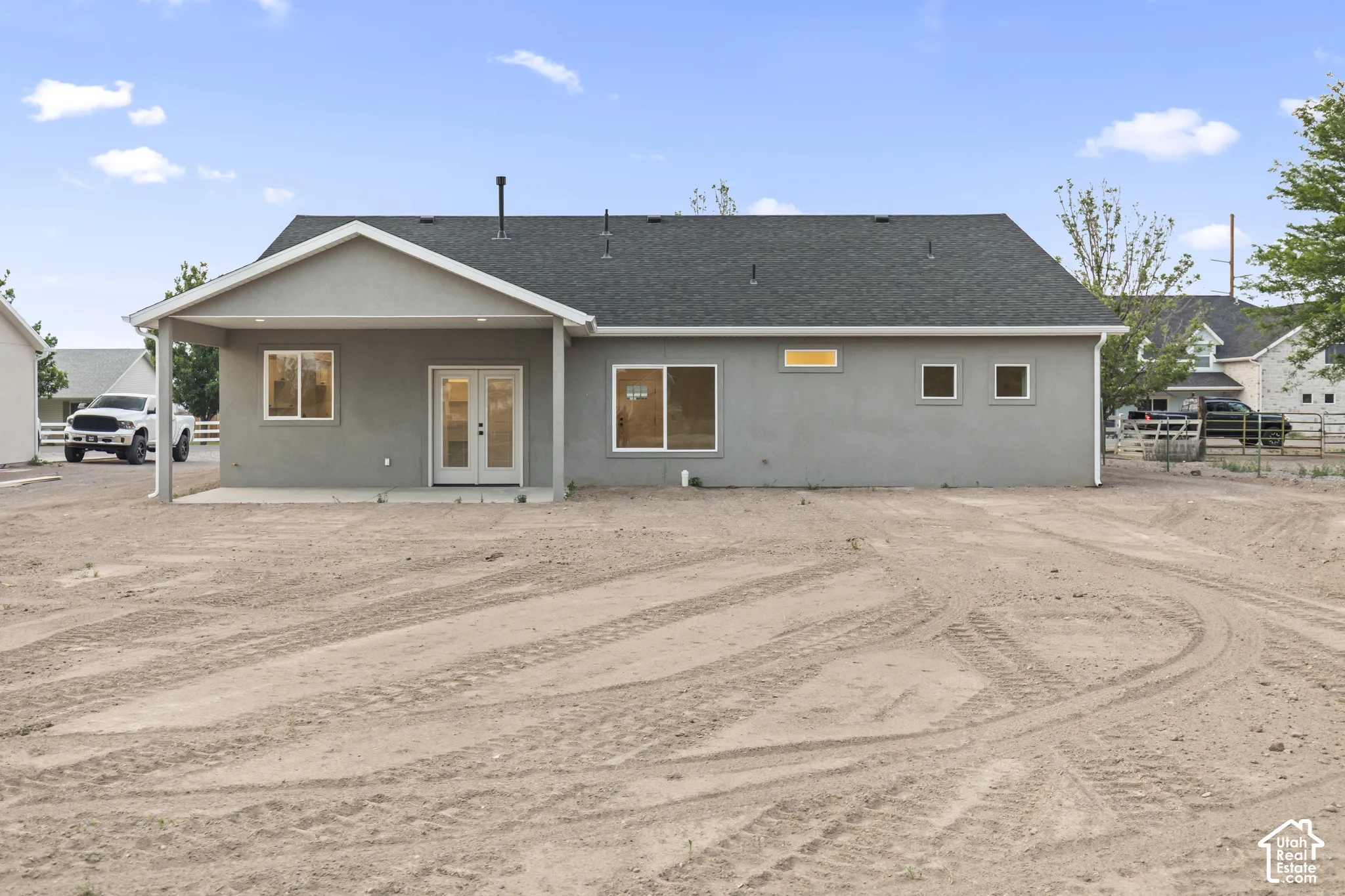 Rear exterior featuring a covered patio with concrete flooring, double French doors, multiple windows, and a dark shingle roof