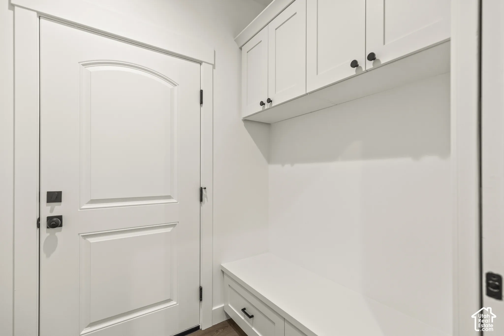 Entryway featuring an arched panel door with matte black hardware, built-in bench seating, upper cabinetry, and wood-finish flooring