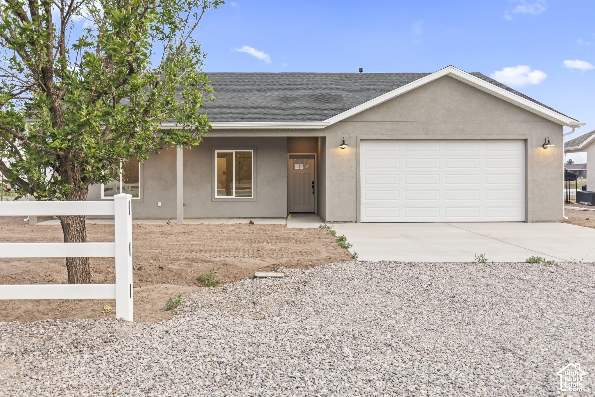 Stucco exterior home featuring a two-car garage, concrete driveway, and a white fence