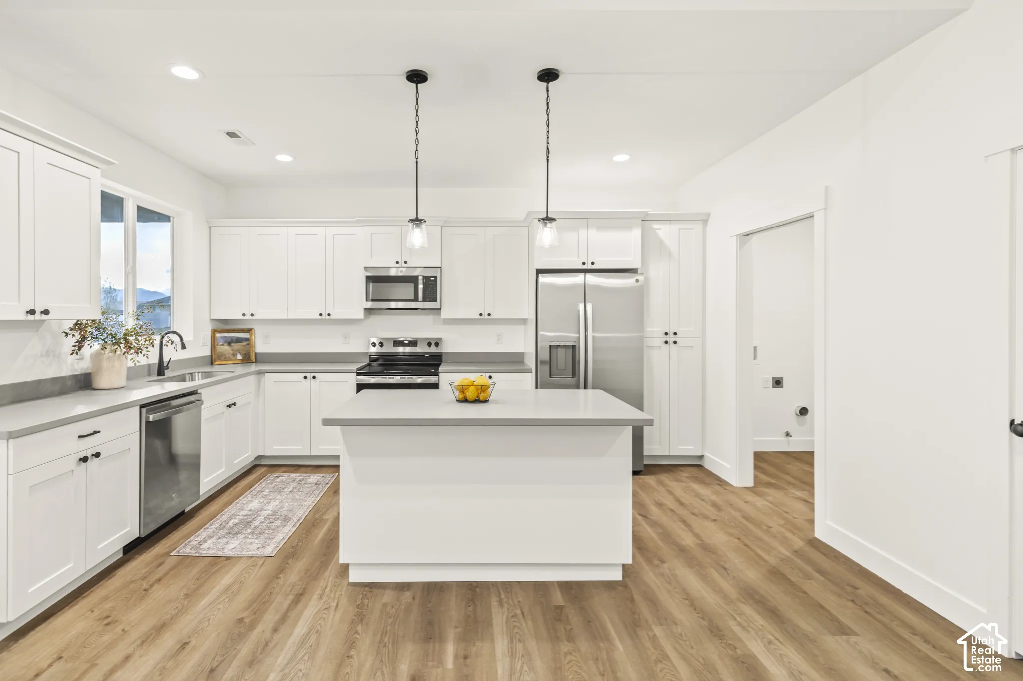 Kitchen featuring white shaker-style cabinetry, a central island with countertop seating, stainless steel appliances, neutral solid-surface countertops, and wood-finish flooring