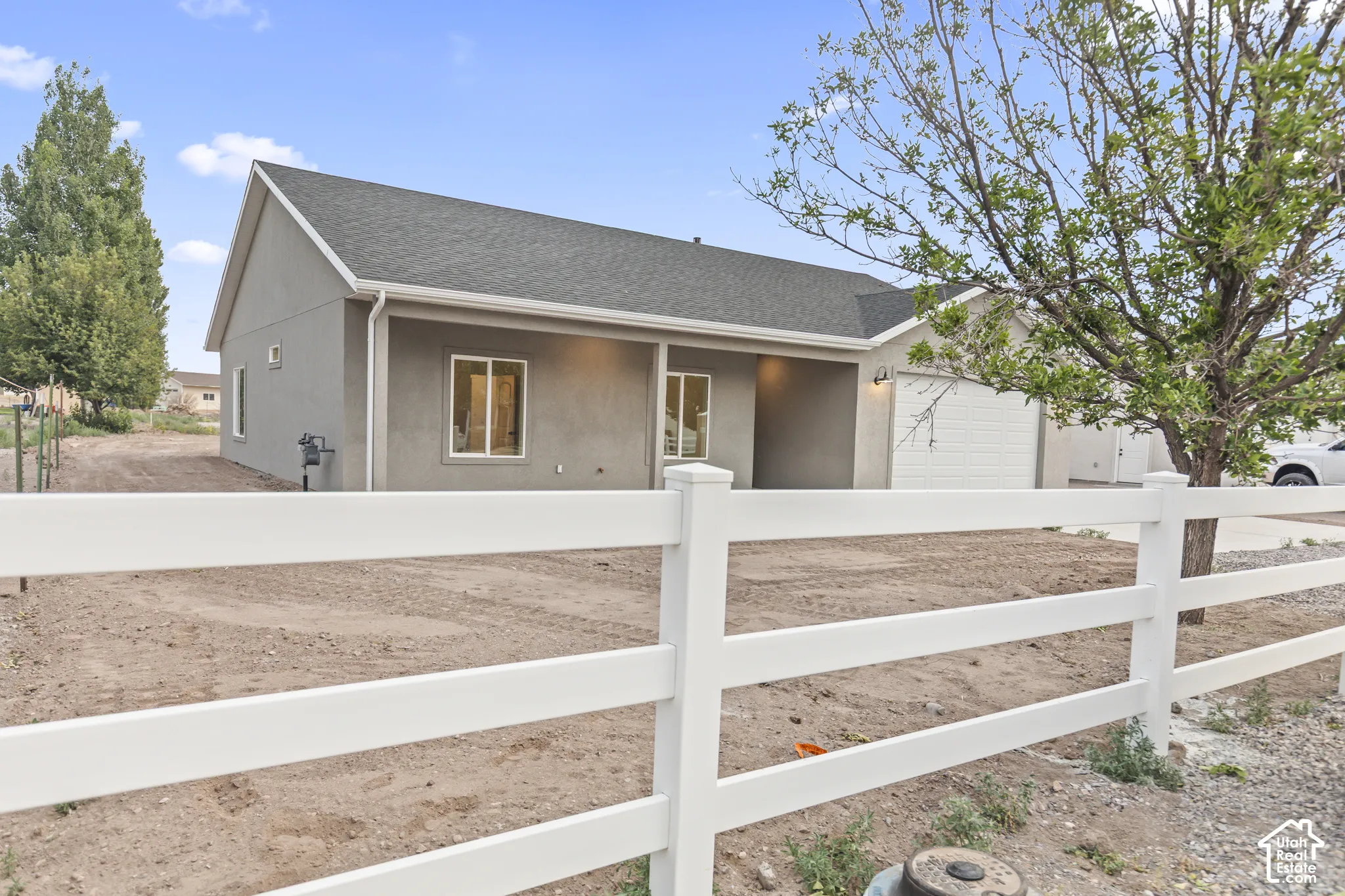 Contemporary ranch-style residence featuring a gray stucco exterior, white trim, and a dark shingle roof